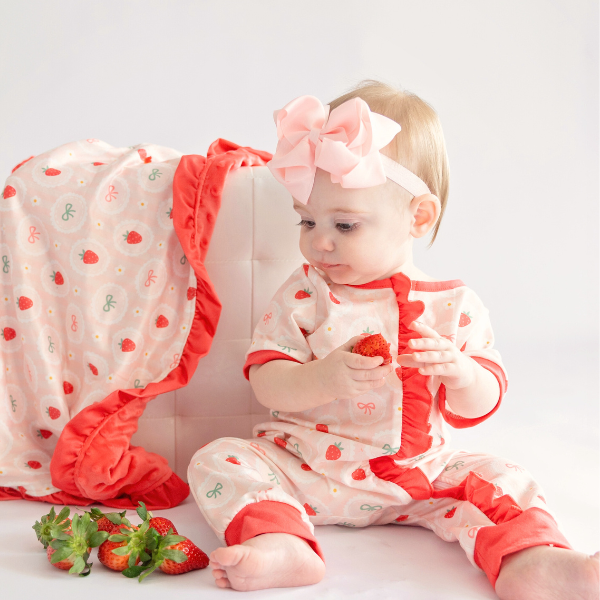 baby wearing strawberry romper next to strawberry blanket
