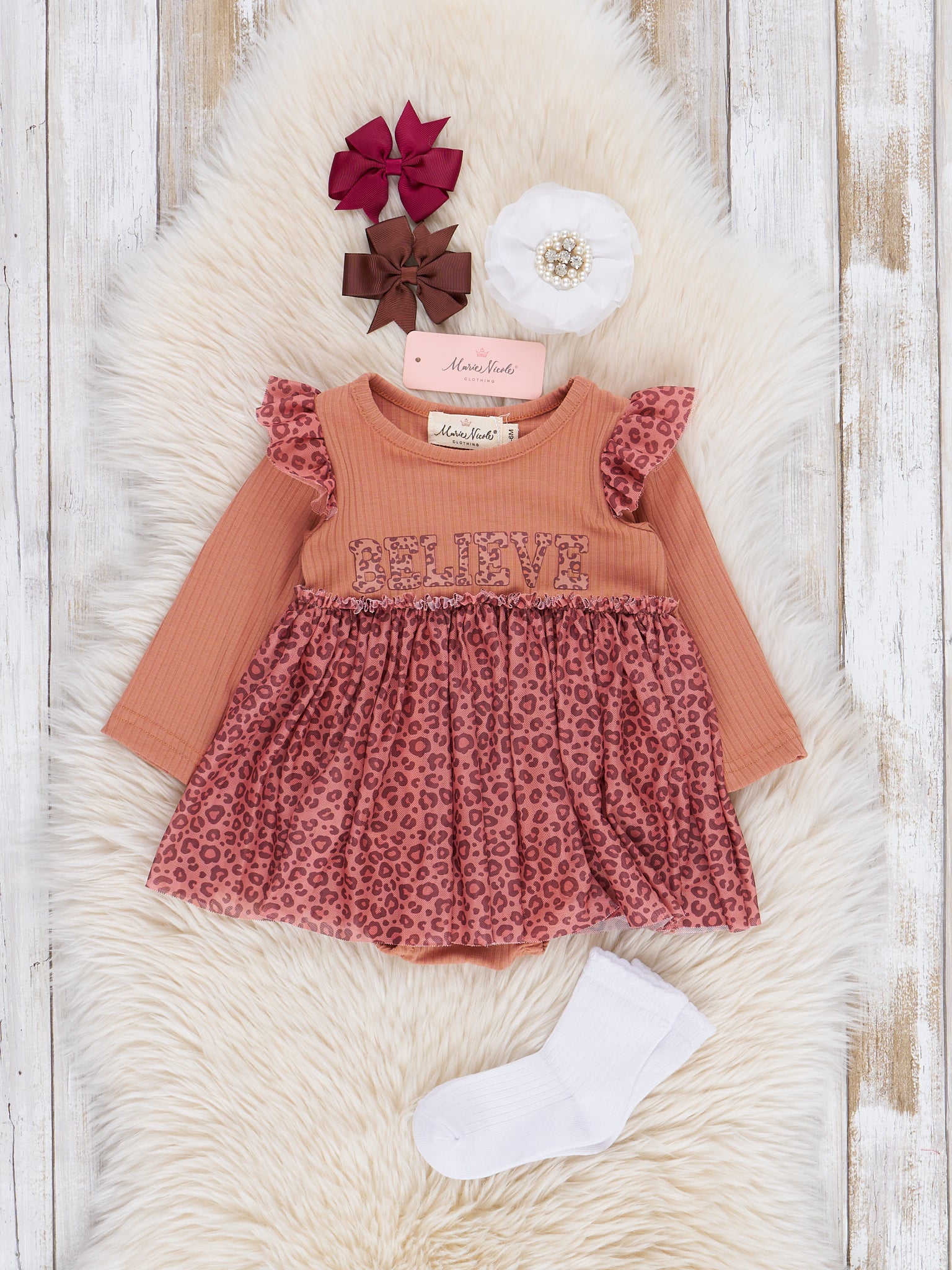 Toddler girl's outfit with peach leopard print tulle overlay and orange long-sleeve top with snap buttons, displayed on a white fuzzy surface, accompanied by a pair of white socks.