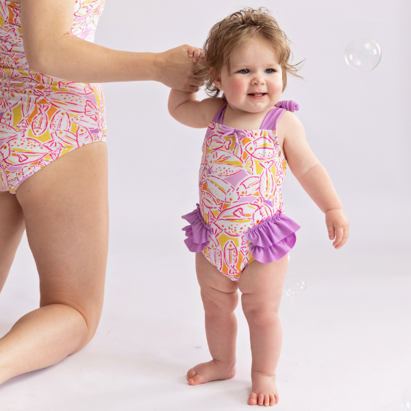 toddler girl stands holding mom's hand wearing matching bathing suits