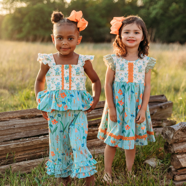 two young girls wear coordinating outfits of blue florals against meadow background